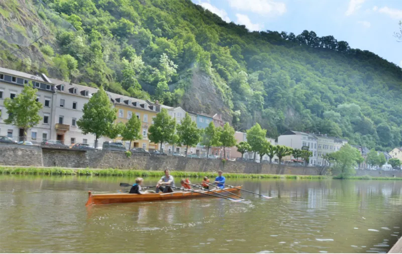Ein Boot mit Ruderern vor dem bewaldeten Hang oberhalb der Lahn