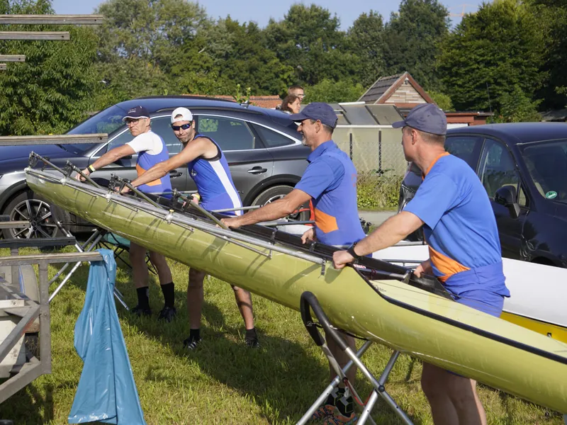 Eine Mannschaft in blauen Trikots trägt ein Boot zum Wasser
