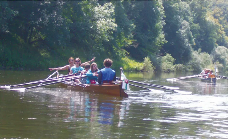 Ein Boot mit mehreren Ruderern nahe dem bewachsenen Ufer der Lahn